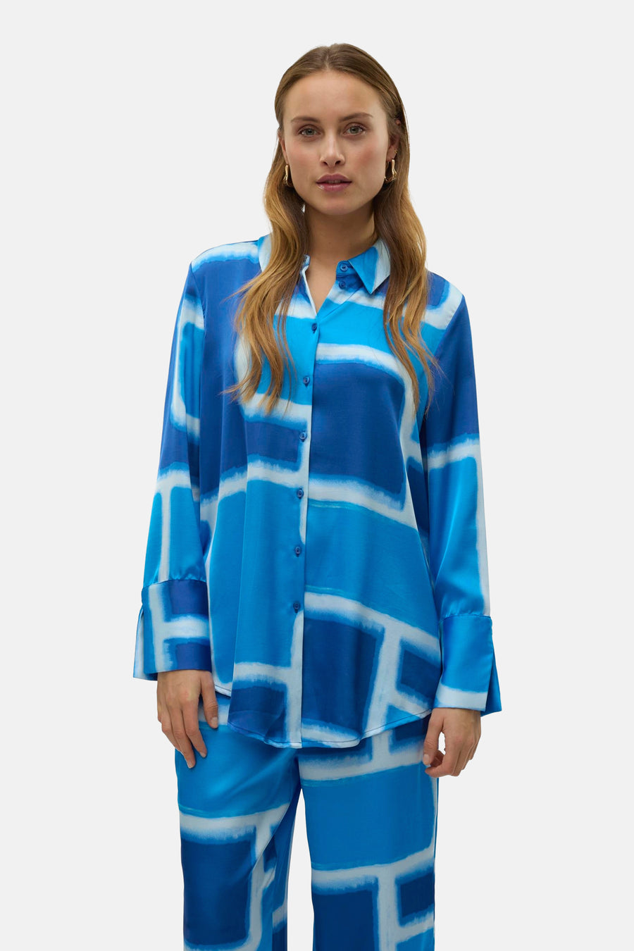 Blauwe blouse met lange mouwen van VERO MODA® met grafische print, knopen en gouden oorbellen.
