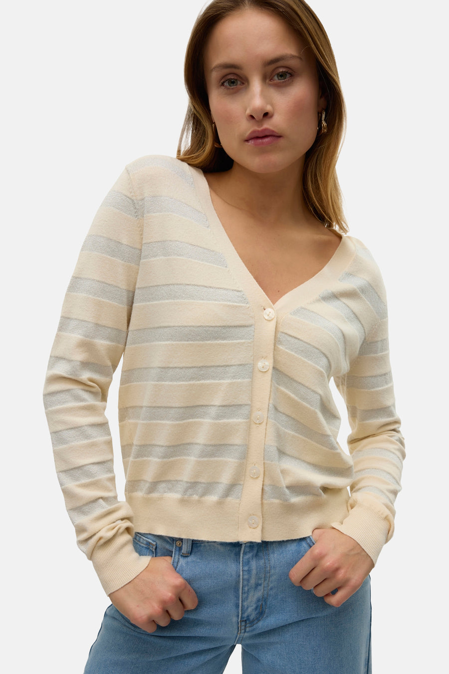 Cardigan beige de VERO MODA avec rayures argentées brillantes et boutons couleur crème, porté avec un jean bleu.
