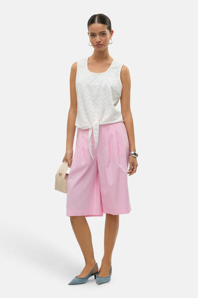 Chemisier sans manches blanc de VERO MODA® avec motif ajouré et détail noué, porté avec un short rose.
