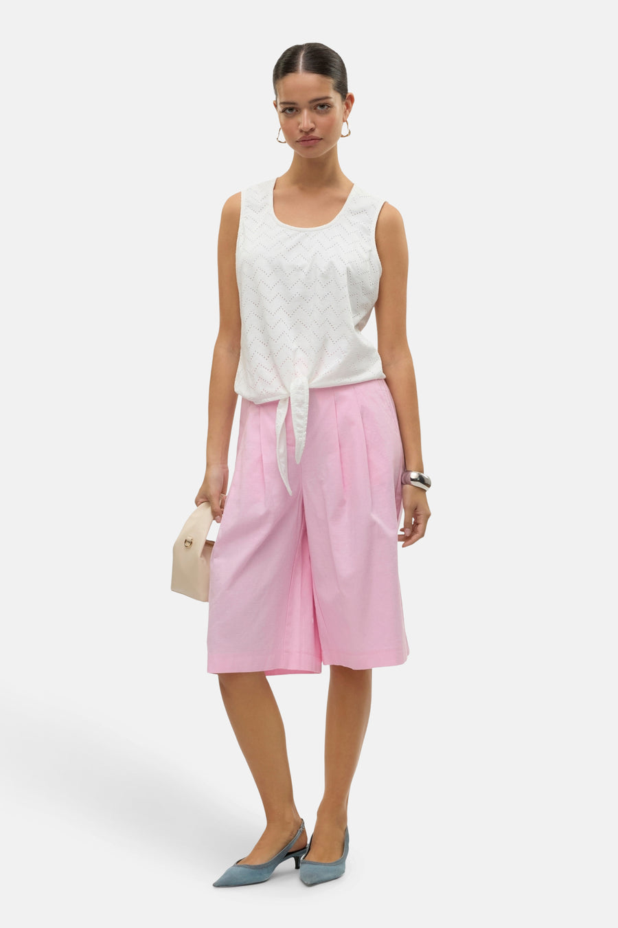 Chemisier sans manches blanc de VERO MODA® avec motif ajouré et détail noué, porté avec un short rose.
