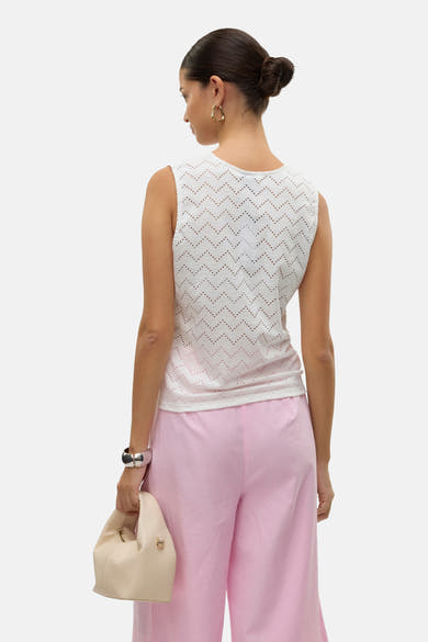 Blouse sans manches blanche ajourée de Vero Moda, avec motif à chevrons, portée avec un pantalon rose et des bijoux dorés.