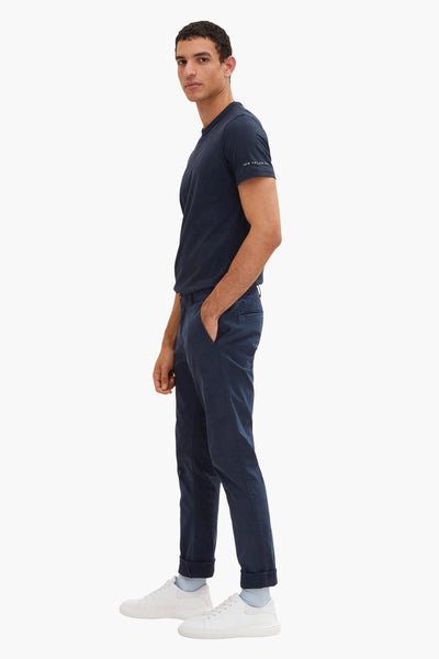 Chino bleu van Tom Tailor, porté avec un t-shirt bleu marine et des baskets blanches, vue de côté.