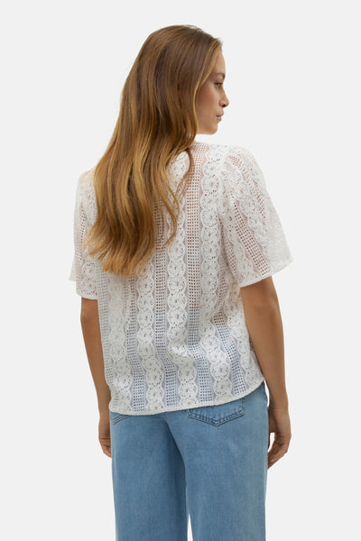 Chemisier blanc à manches courtes de VERO MODA, en dentelle ajourée, porté avec un jean bleu.