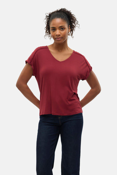 T-shirt à manches courtes rouge by VERO MODA, avec des détails en dentelle aux épaules, porté avec un jean bleu foncé.
