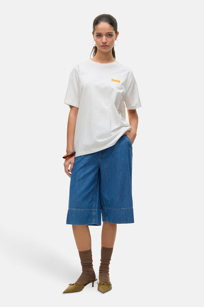 T-shirt blanc de VERO MODA avec un logo "Soleil" brodé, porté avec un short en jean bleu et des accessoires marron.
