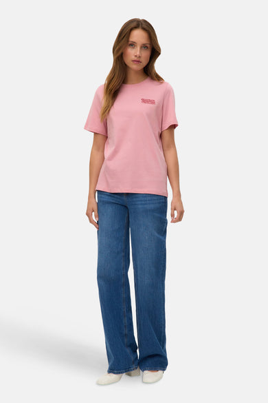 T-shirt rose à manches courtes de VERO MODA, porté avec un jean bleu ample et des ballerines blanches.
