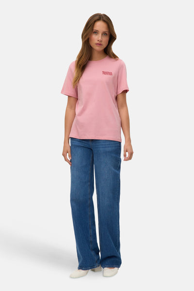 T-shirt rose à manches courtes de VERO MODA, porté avec un jean bleu ample et des ballerines blanches.
