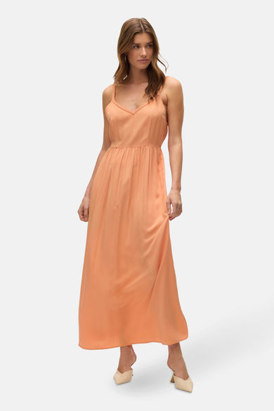 Robe longue orange de VERO MODA®, avec bretelles fines et ourlet flottant, portée avec des chaussures claires.
