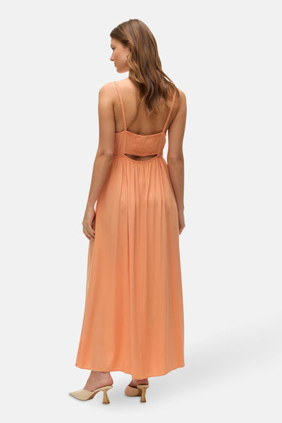 Robe longue orange de VERO MODA® avec des bretelles tressées et une découpe dans le dos, portée avec des mules beiges.

