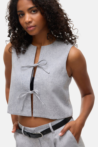 Chemisier gris à manches courtes de VERO MODA®, avec des détails noués et porté avec une ceinture noire.
