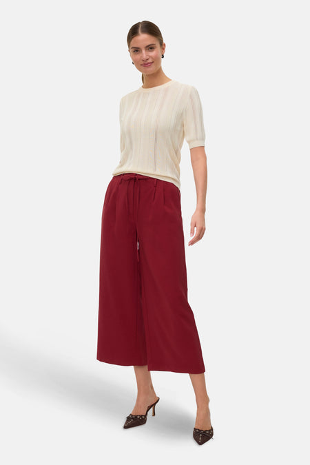 Rode broek van VERO MODA®, losse pasvorm met trekkoord, gedragen met een crèmekleurige top en bruine pumps.
