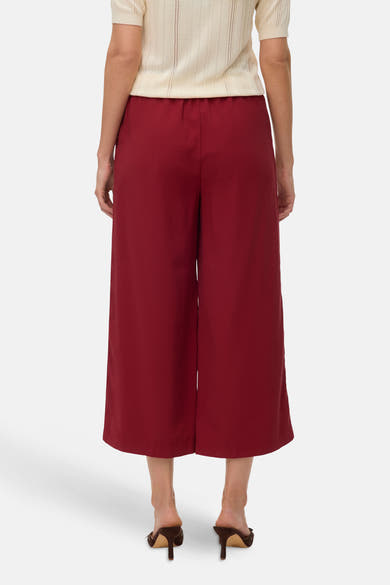 Rode broek van VERO MODA, wijde pasvorm, gedragen met een gebroken wit gebreid kledingstuk met korte mouwen en bruine muiltjes met hak.