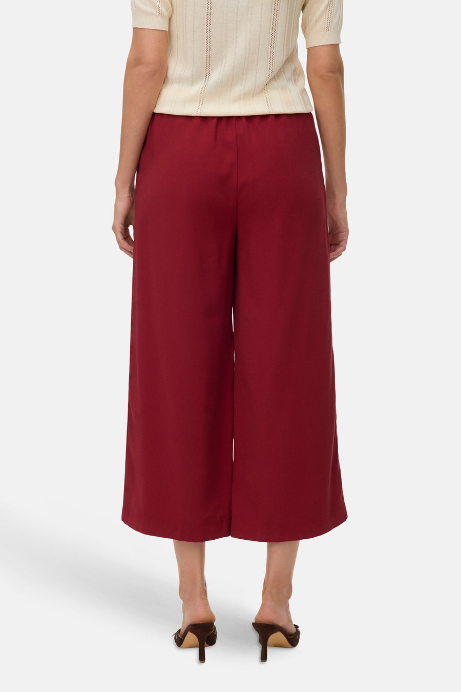 Rode broek van VERO MODA, wijde pasvorm, gedragen met een gebroken wit gebreid kledingstuk met korte mouwen en bruine muiltjes met hak.