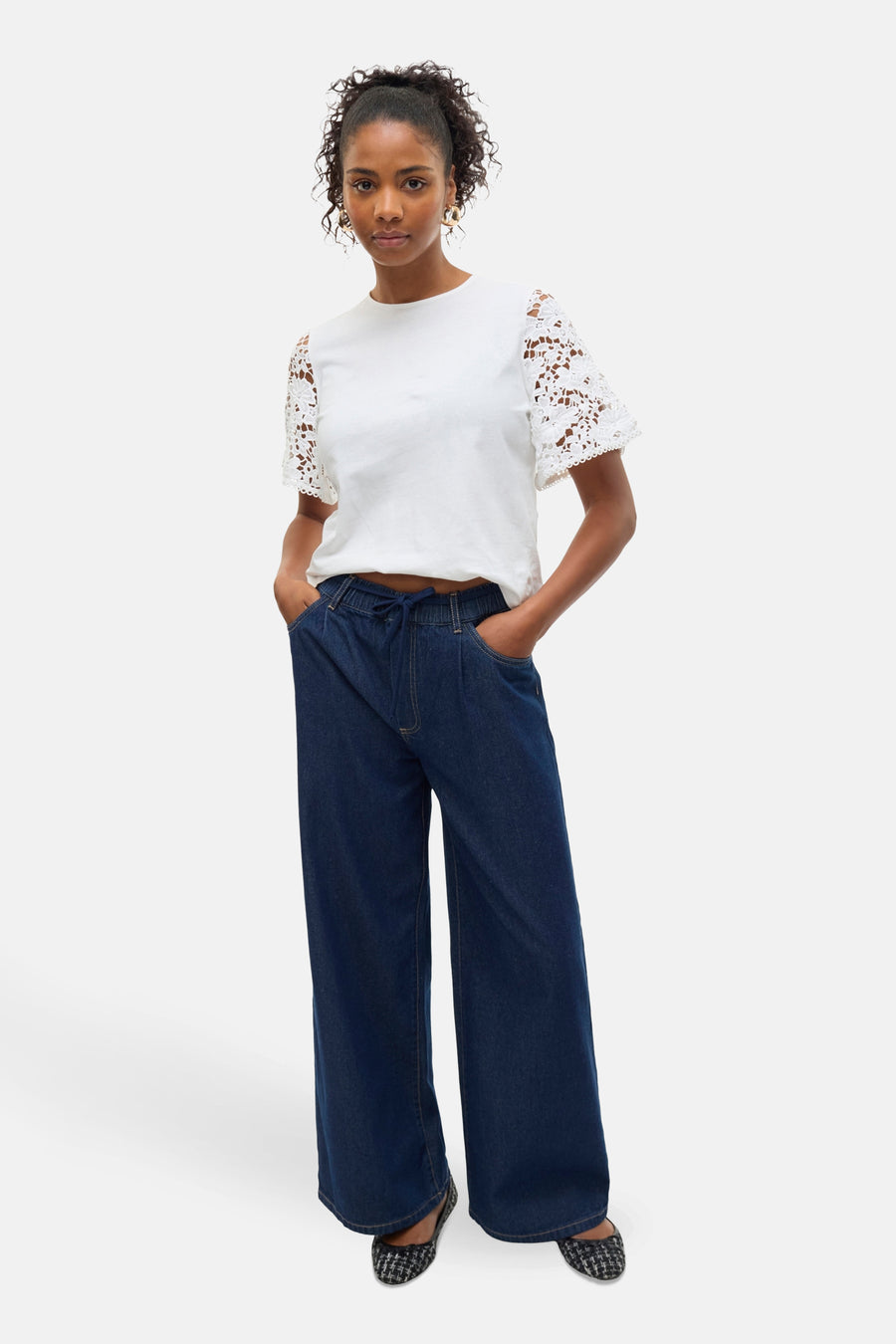 Jean large en denim bleu foncé de VERO MODA, porté avec un t-shirt blanc à manches en dentelle.
