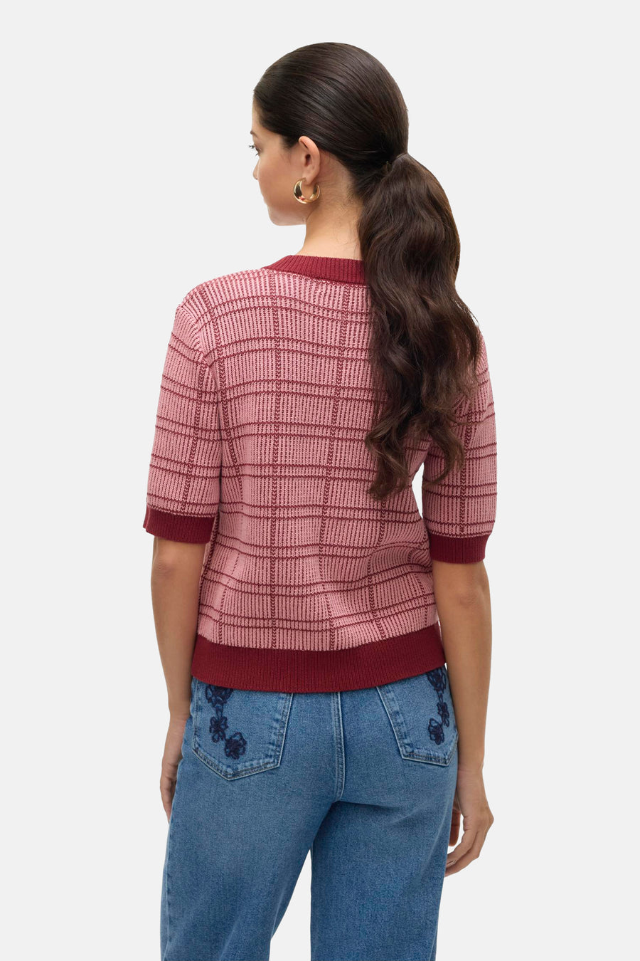 Rode rondehals trui met ruitpatroon van VERO MODA, gedragen met een blauwe spijkerbroek met borduursel op de achterkant.