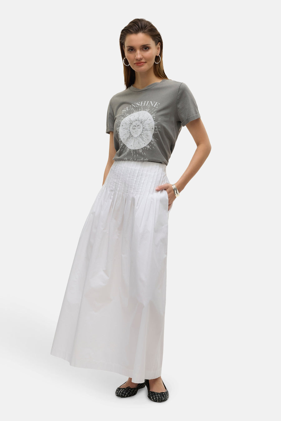 Jupe longue blanche de VERO MODA, plissée avec poches, portée avec un t-shirt imprimé et des ballerines à motifs.
