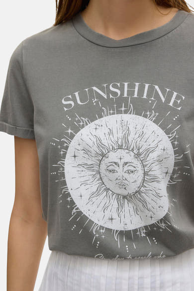 Jupe longue blanche de VERO MODA, avec un plissé fin et portée avec un t-shirt gris imprimé soleil.
