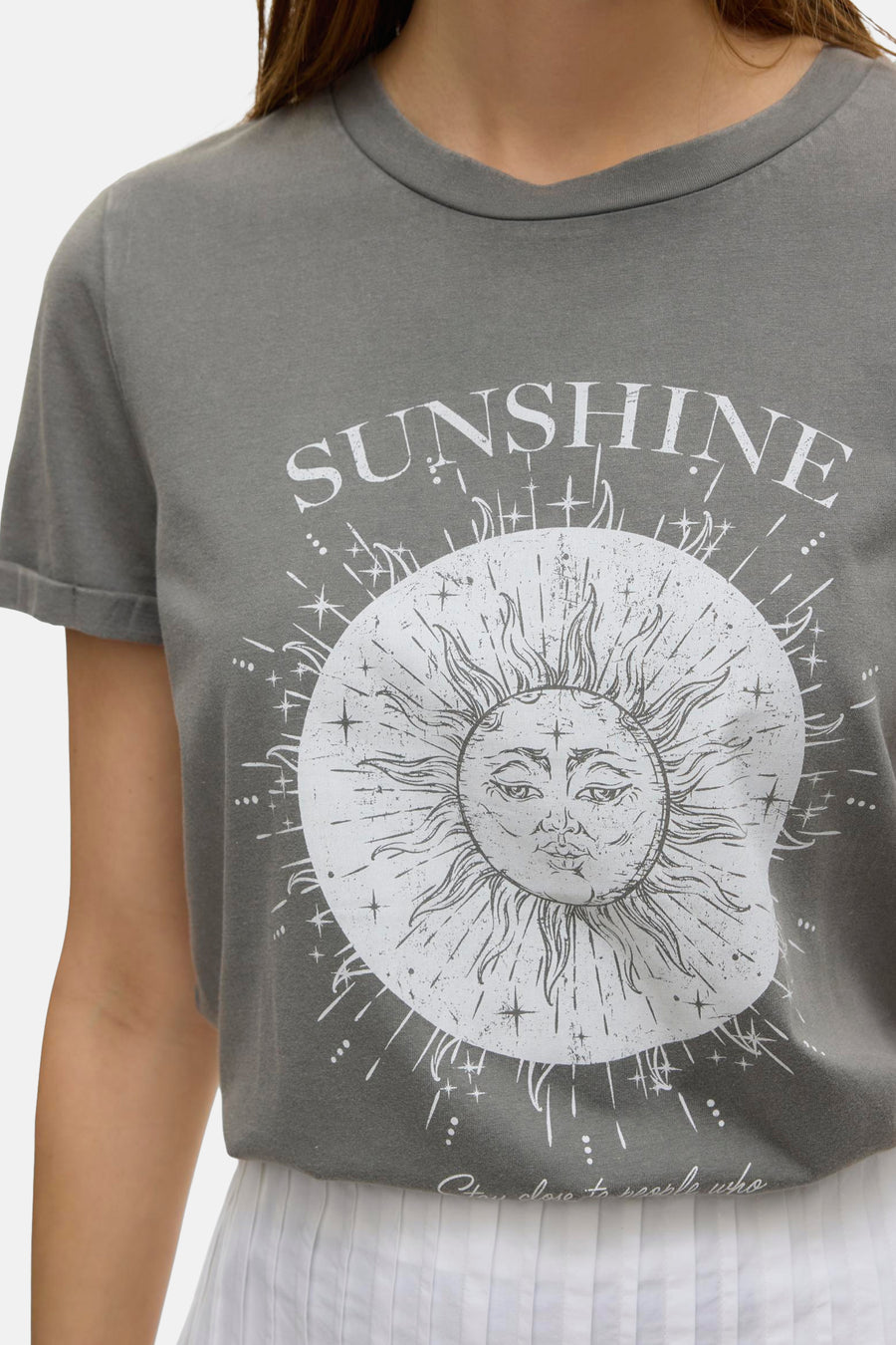 Jupe longue blanche de VERO MODA, avec un plissé fin et portée avec un t-shirt gris imprimé soleil.
