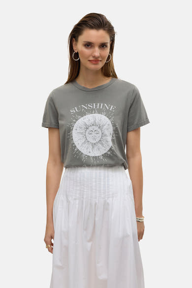Jupe longue blanche de VERO MODA, avec plis et ourlet tombant, portée avec un t-shirt imprimé soleil et des créoles argentées.
