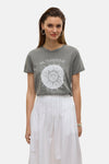 Jupe longue blanche de VERO MODA, avec plis et ourlet tombant, portée avec un t-shirt imprimé soleil et des créoles argentées.
