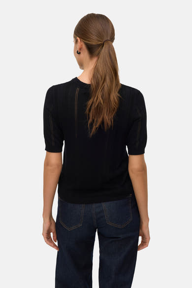 Pull à col rond noir de Vero Moda, avec manches courtes et motif ajouré vertical, porté avec un jean.