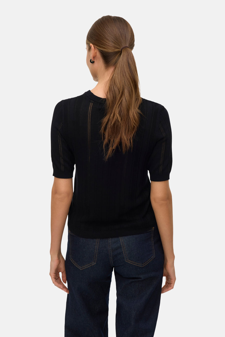 Pull à col rond noir de Vero Moda, avec manches courtes et motif ajouré vertical, porté avec un jean.