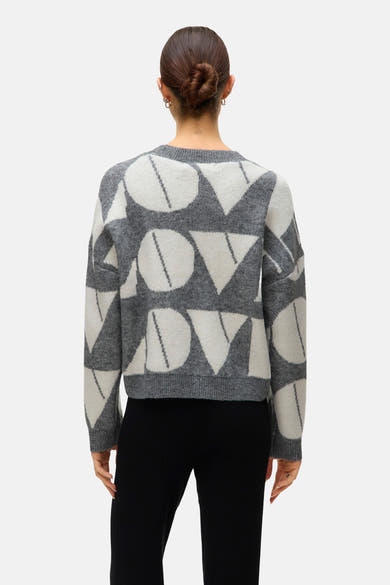 Grijze trui met ronde hals van VERO MODA, met contrasterend geometrisch patroon, gedragen met een zwarte broek.