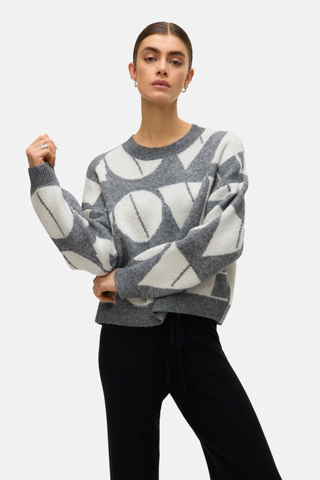 Pull à col rond gris de VERO MODA avec motifs graphiques, porté avec un pantalon noir.