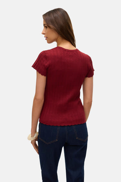 T-shirt rouge à manches courtes de VERO MODA, avec texture côtelée et ourlet ondulé, porté avec un jean foncé.