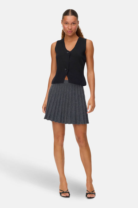 Grijze gemêleerde korte rok van VERO MODA, geplooid, gedragen met een zwarte top en sandalen.