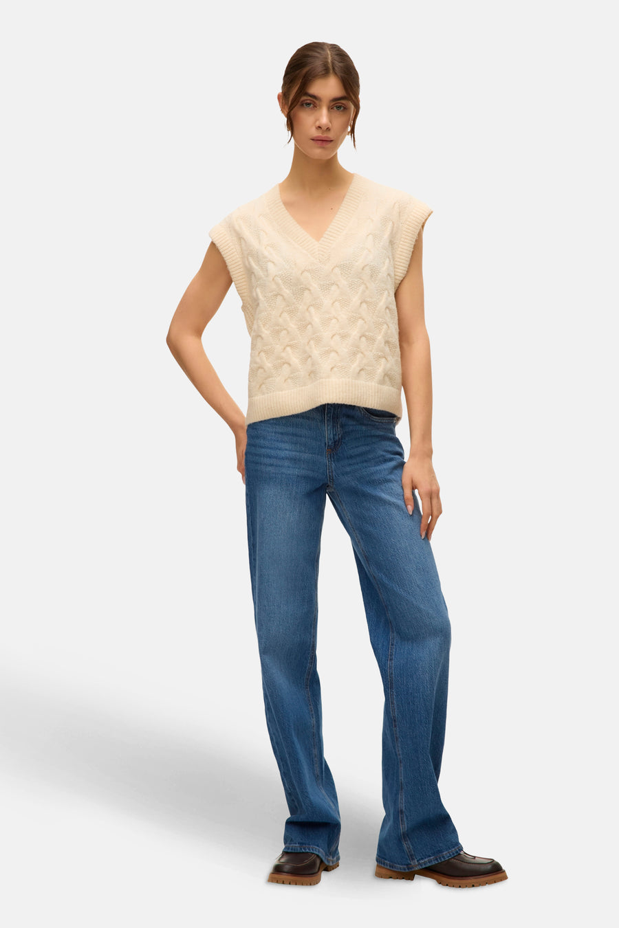 Débardeur beige en tricot torsadé de VERO MODA®, porté avec un jean bleu et des chaussures marron.
