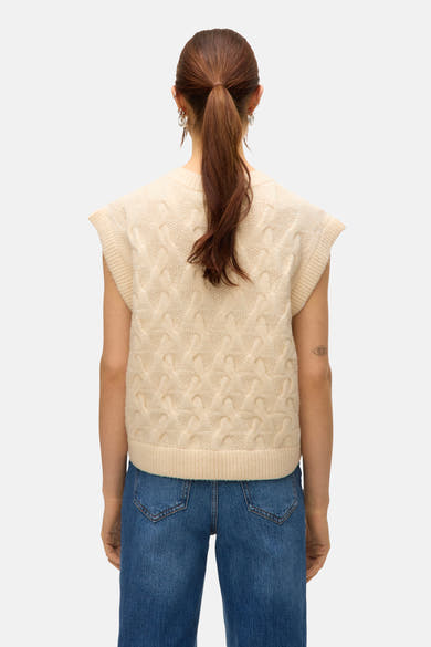 Débardeur en tricot beige de Vero Moda, avec motif torsadé visible de dos, porté avec un jean bleu.