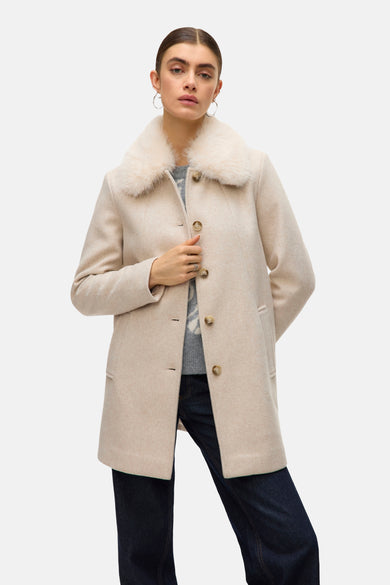Ecru korte jas van Vero Moda met imitatiebontkraag, gedragen met een trui met patroon en een donkere jeans.