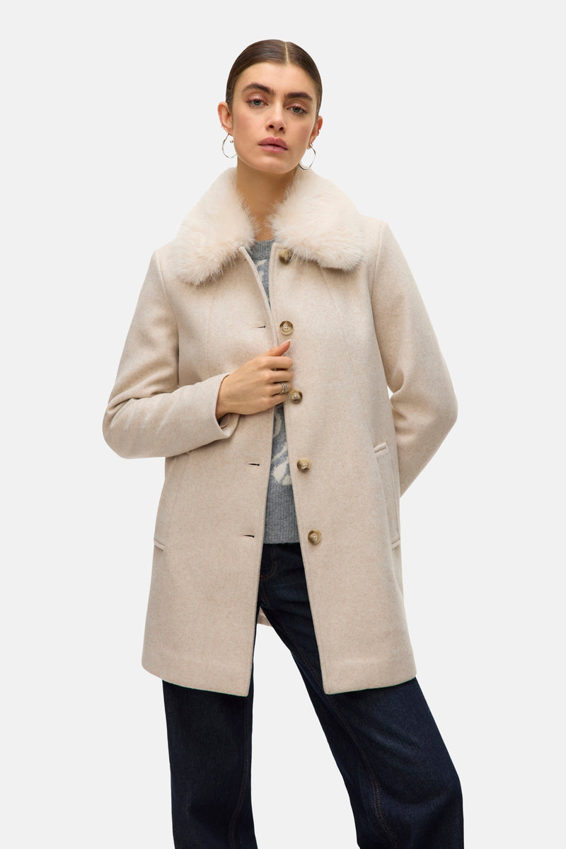 Ecru korte jas van Vero Moda met imitatiebontkraag, gedragen met een trui met patroon en een donkere jeans.