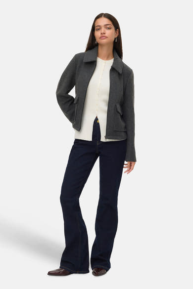 Kort grijs jasje van VERO MODA®, gedragen met een witte gebreide cardigan met knopen en een donkerblauwe flared jeans.