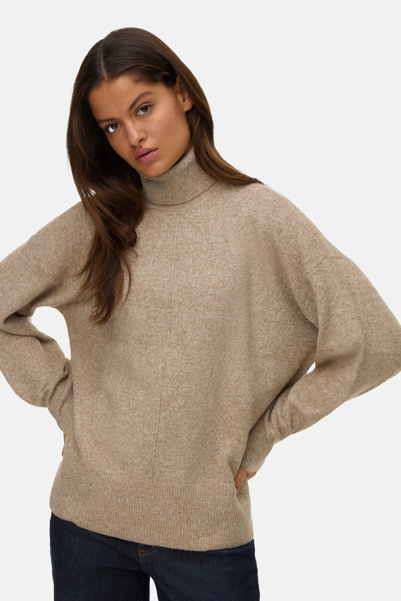 Pull à col roulé beige de VERO MODA, avec un motif chiné et porté avec un jean foncé.
