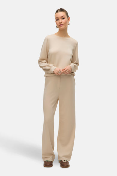 Pantalon écru de Vero Moda, coupe ample, porté avec un pull assorti et des chaussures marron.