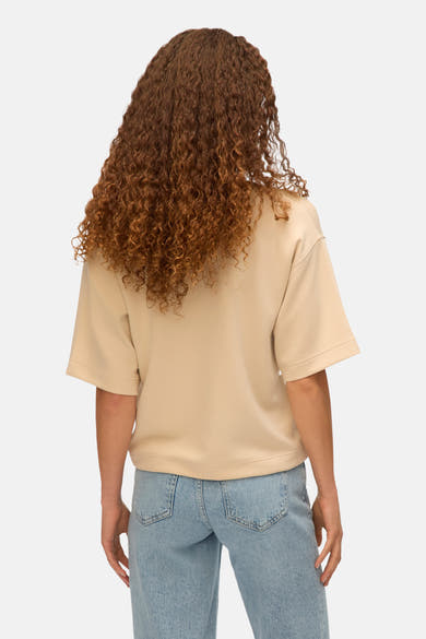 T-shirt écru à manches courtes de VERO MODA, porté avec un jean bleu, vue de dos, avec des cheveux longs bouclés.
