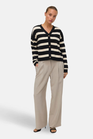 Cardigan rayé noir et écru de Vero Moda, porté avec un pantalon beige ample et des sandales noires.
