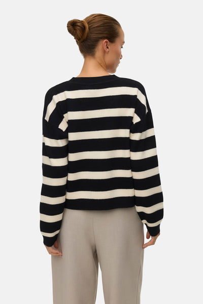 Cardigan multicolore de VERO MODA, à rayures horizontales noires et beiges, porté avec un pantalon beige uni.
