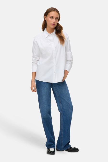 Wit overhemd met lange mouwen van Vero Moda, met geborduurd bloemenpatroon en gedragen met een blauwe spijkerbroek.