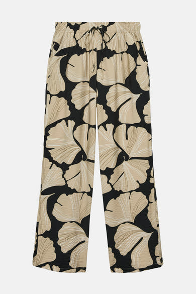 Multikleurige broek van VERO MODA® met een beige bladmotief op een zwarte achtergrond, losse pasvorm en elastische tailleband.