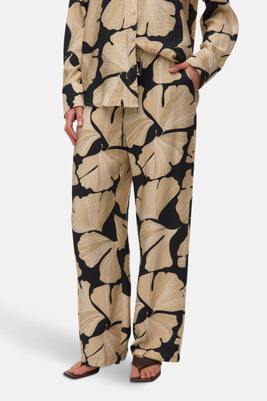 Multikleurige broek van VERO MODA® met een beige en zwart bloemenpatroon, gedragen met donkerbruine sandalen.