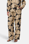 Multikleurige broek van VERO MODA® met een beige en zwart bloemenpatroon, gedragen met donkerbruine sandalen.