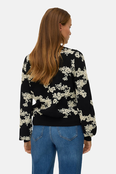 Pull col rond noir de VERO MODA, à motifs floraux blancs texturés, porté avec un jean bleu.
