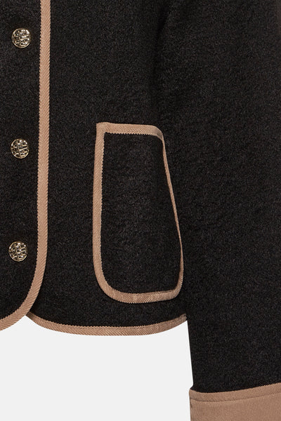 Veste courte noire par VERO MODA, avec bordure contrastée et poche passepoilée.