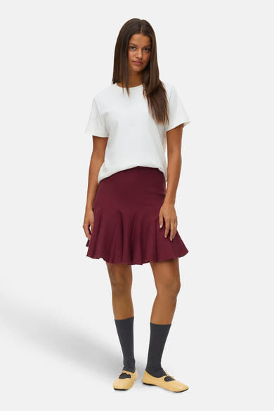 Korte bordeauxrode rok van VERO MODA, skatermodel, gedragen met een wit T-shirt en hoge grijze sokken.