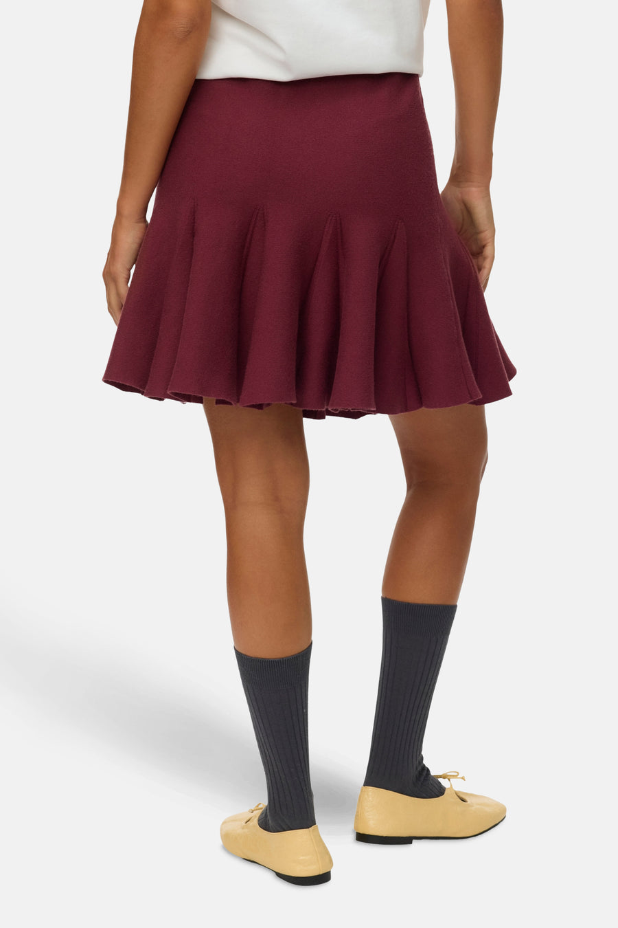 Korte bordeauxrode rok van VERO MODA, uitlopende pasvorm, gedragen met grijze sokken en crèmekleurige platte schoenen.