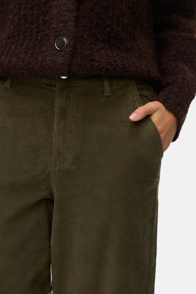 Kaki corduroy broek van VERO MODA, met een hand in de zak, gedragen met een bruine cardigan.