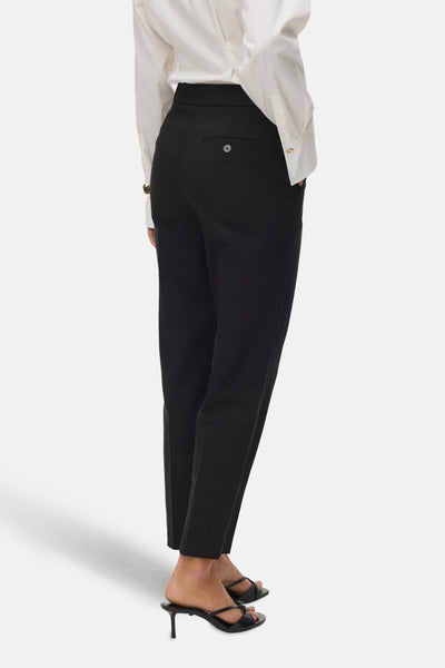 Pantalon noir de VERO MODA, avec une poche boutonnée à l'arrière, porté avec une chemise blanche et des mules à talons.